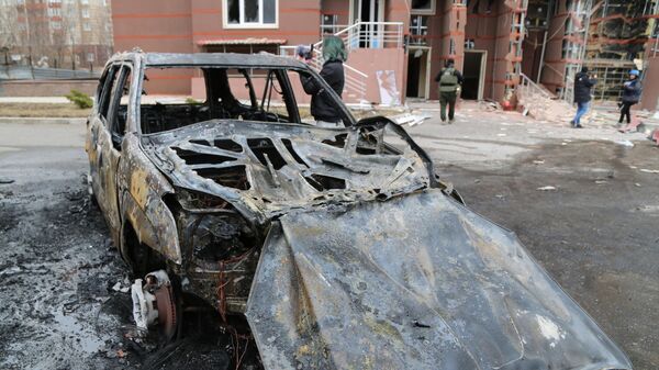 Сгоревший автомобиль во дворе многоэтажного жилого дома в Донецке, поврежденного в результате обстрела
