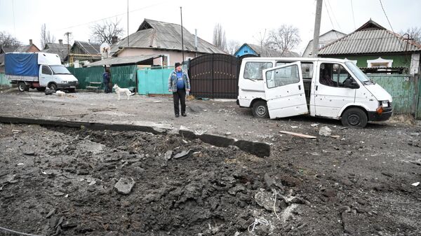 Воронка от взрыва и поврежденный в результате обстрела автомобиль в Киевском районе Донецка