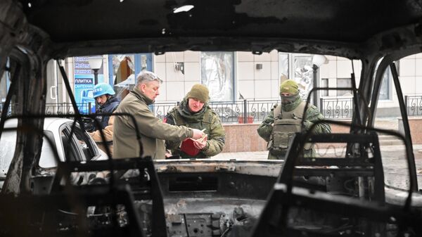 Сотрудники военной комендатуры у сгоревшего в результате обстрелов автомобиля в Киевском районе Донецка