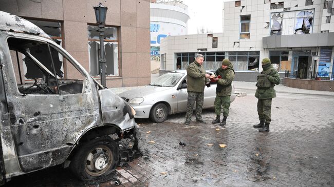 Сотрудники военной комендатуры у сгоревшего в результате обстрелов автомобиля в Киевском районе Донецка