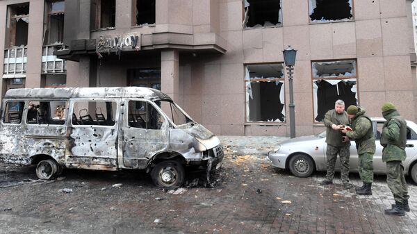 Сотрудники военной комендатуры у сгоревшего в результате обстрелов автомобиля в Киевском районе Донецка
