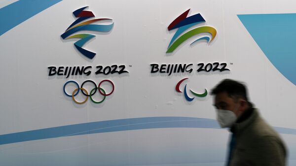 Мужчина в маске проходит мимо логотипов Зимних Олимпийских и Паралимпийских игр 2022 года, Пекин.