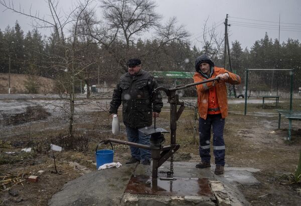 Мужчины набирают питьевую воду в различные емкости во дворе жилого дома в освобожденном городе Счастье в Луганской народной республике