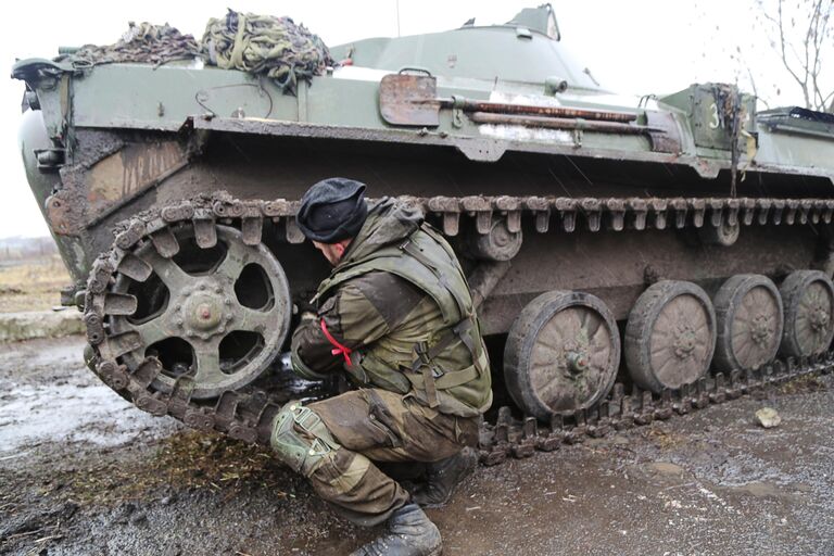 Военнослужащий армии ДНР чинит бронетехнику на дороге в селе Бугас