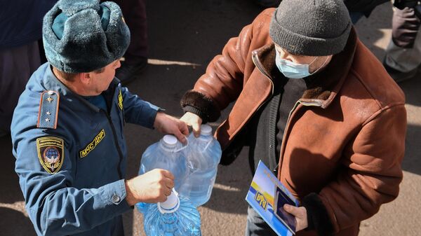 Сотрудник МЧС ДНР передает бутыли воды из гуманитарной помощи жителю села Бугас