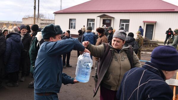 Сотрудник МЧС ДНР передает бутыли воды из гуманитарной помощи жительнице села Бугас