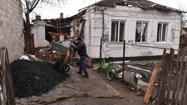 Мужчина разгружает тележку с углем у разрушенного дома в селе Талаковка в Донецкой народной республике