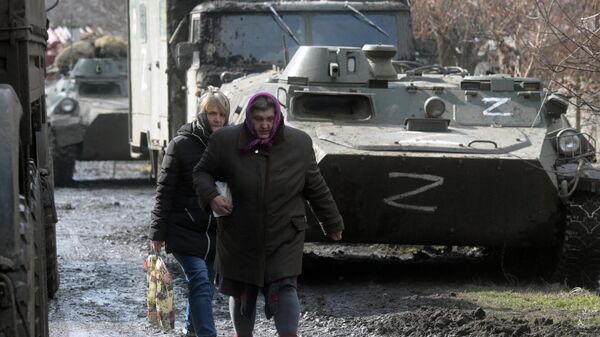 Местные жительницы проходят около колонны военной техники в селе Свободное Донецкой народной республики