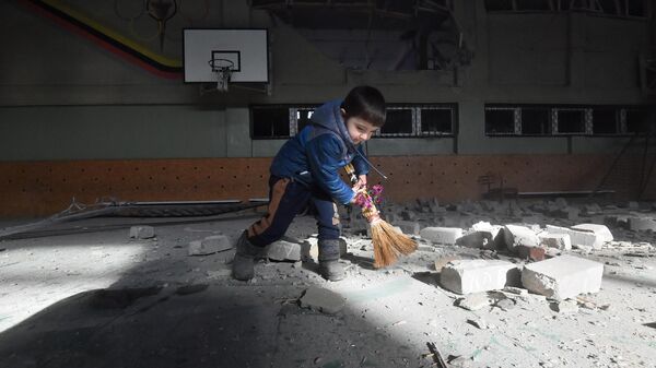 Ребенок подметает мусор в разрушенном спортивном зале школы в поселке Сартана в Донецкой народной республике