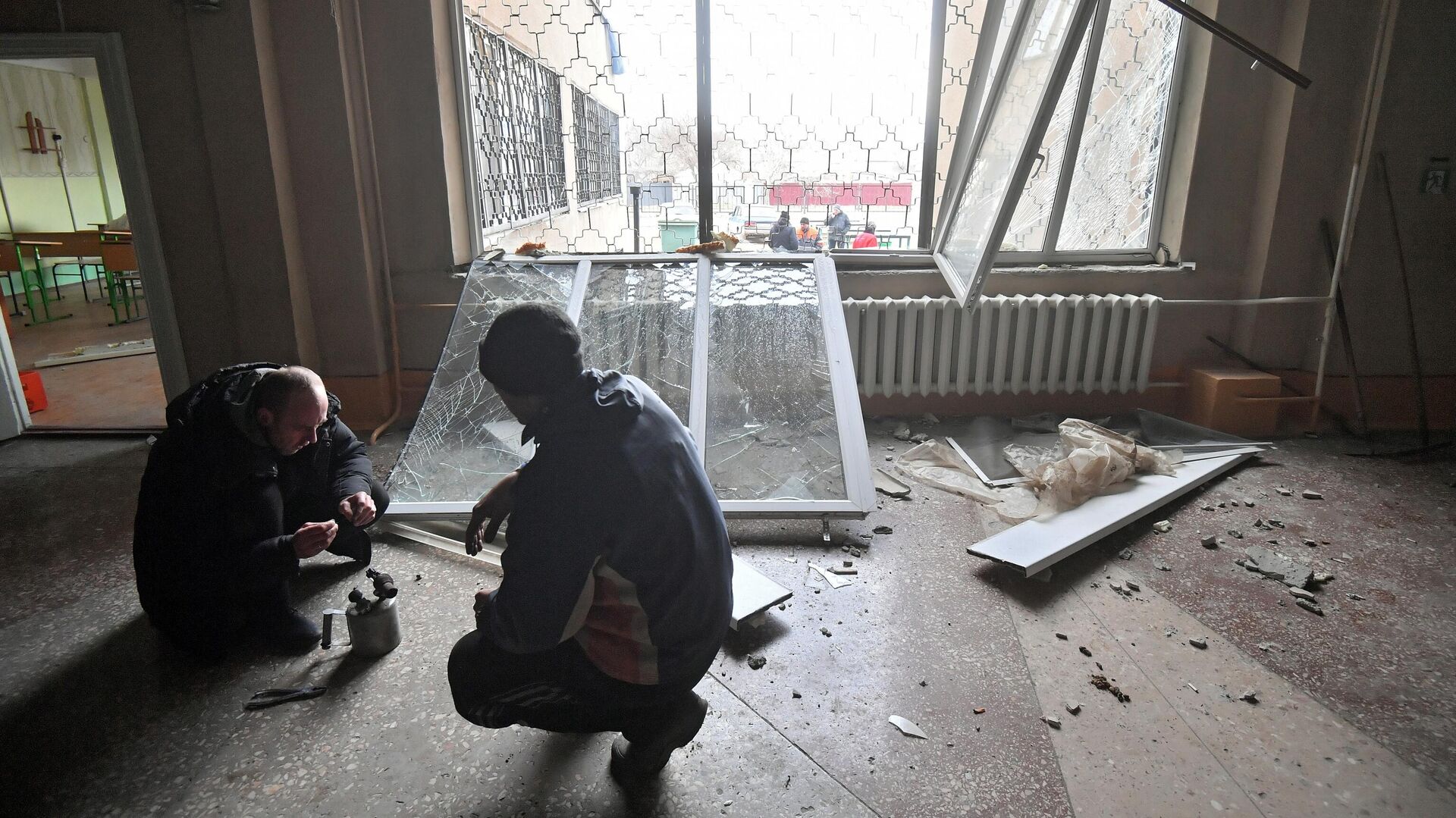 Мужчины ремонтируют выбитые взрывами окна в здании школы в Донецкой народной республике - РИА Новости, 1920, 14.03.2022