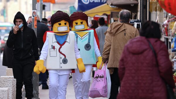 Люди, одетые как фигурки врачей Lego, проходят мимо магазинов в Иерусалиме, за день до еврейского праздника Пурим.