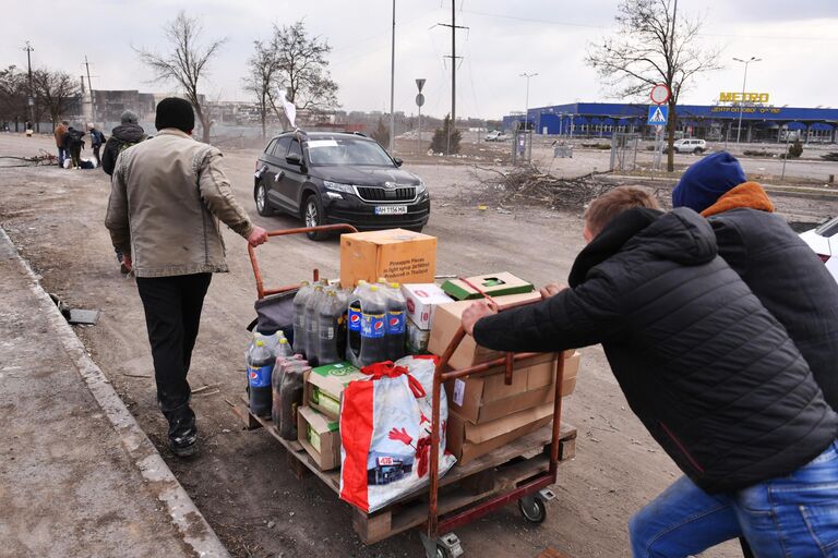 Местные жители везут тележку с продуктами возле магазина Metro в Мариуполе