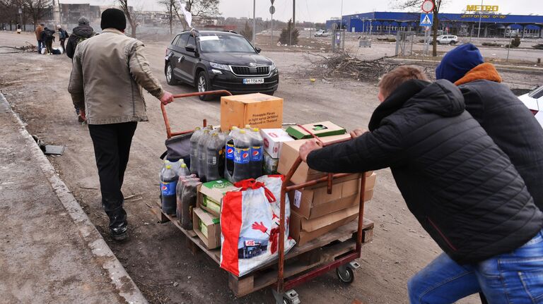 Местные жители везут тележку с продуктами возле магазина Metro в Мариуполе
