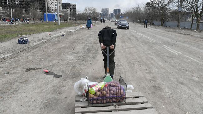 Мужчина везет тележку с продуктами на дороге в Мариуполе