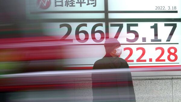 Мужчина в защитной маске стоит перед электронным табло с ценами на бирже, Токио