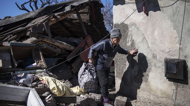 Женщина во дворе своего дома, пострадавшего в результате обстрела, в городе Брянка