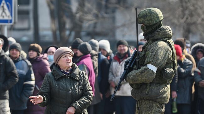 Женщина из очереди, где люди ожидают выдачу гуманитарной помощи, разговаривает с военнослужащим