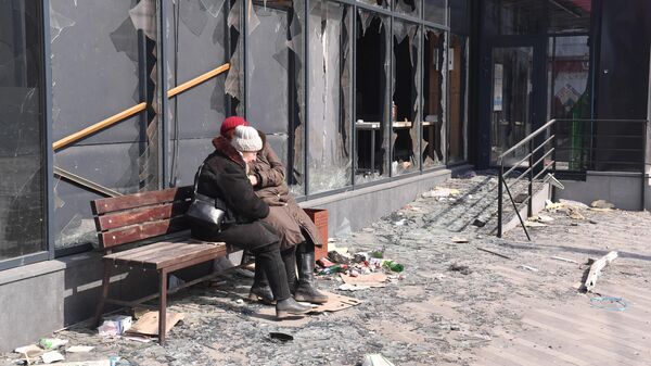 Женщины сидят на лавочке возле разбитого магазина в Мариуполе