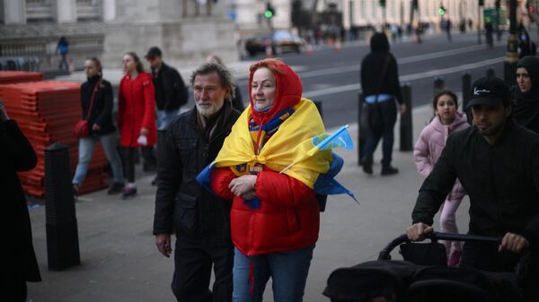 Женщина с флагом Украины, накинутом на плечи, идет по улице в Лондоне 