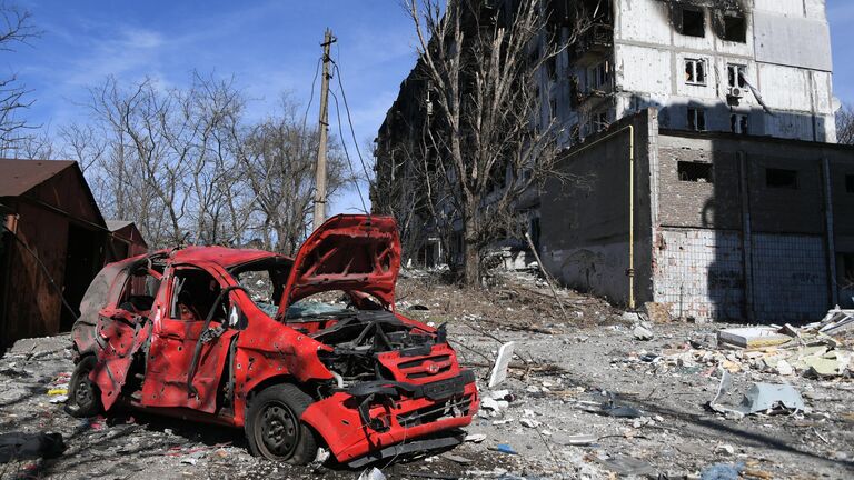 Уничтоженный автомобиль во дворе разрушенного в результате обстрелов жилого дома в Мариуполе