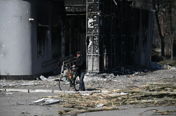 Мужчина с велосипедом во дворе разрушенного в результате обстрелов жилого дома в Мариуполе