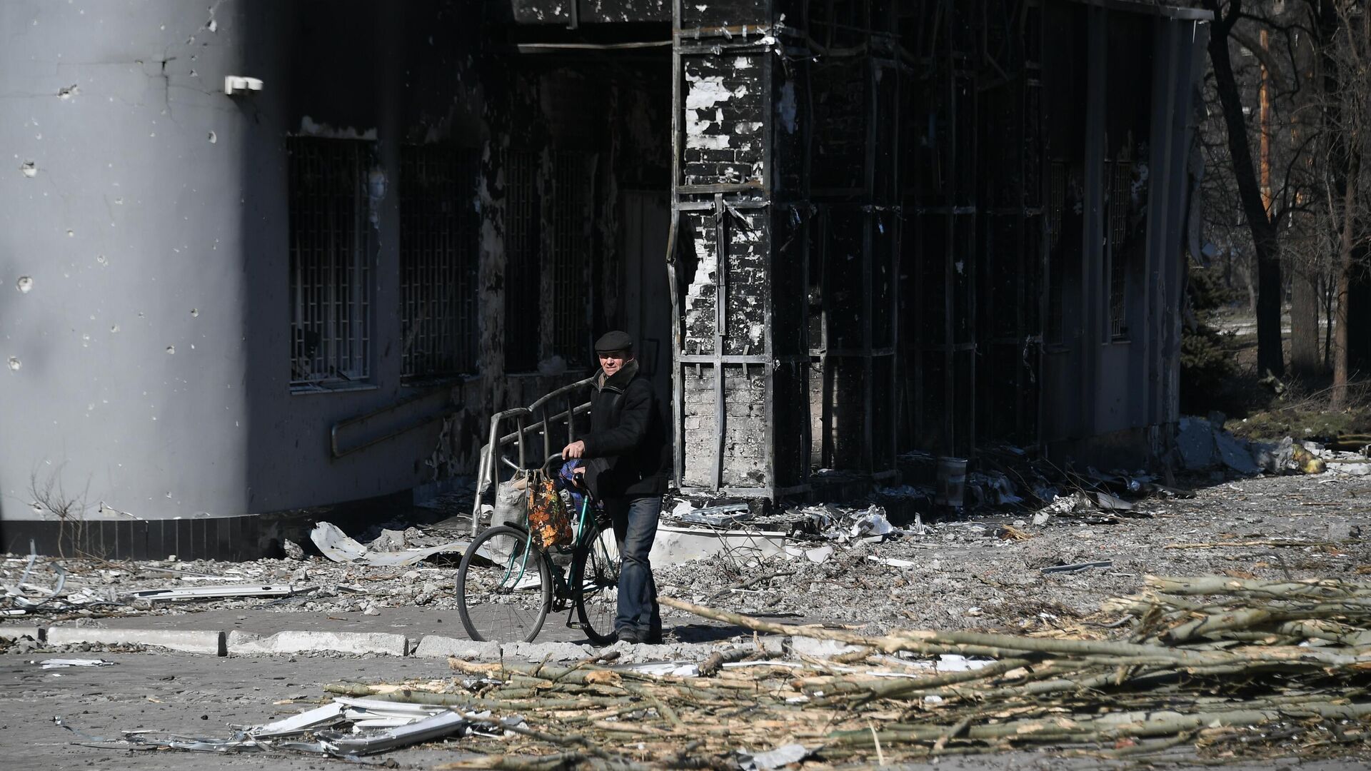 Мужчина с велосипедом во дворе разрушенного в результате обстрелов жилого дома в Мариуполе - РИА Новости, 1920, 29.03.2022