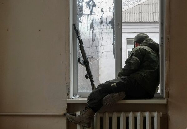 Военнослужащий ДНР сидит у окна во время боестолкновений в Левобережном районе Мариуполя