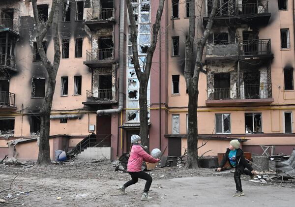 Дети играют в мяч во дворе разрушенного дома в Мариуполе