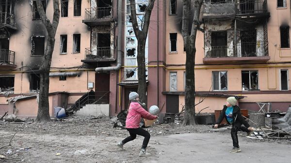 Дети играют в мяч во дворе разрушенного дома в Мариуполе