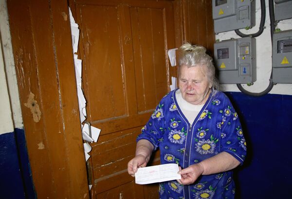 Пожилая женщина показывает многочисленные счета за коммунальные услуги жильцам, бросившим жилье из-за обстрелов в поселке шахты Глубокая в Горловке.
