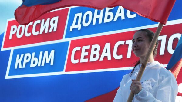 Девушка держит в руках флаг на праздничном митинге в честь восьмилетия провозглашения ДНР и ЛНР