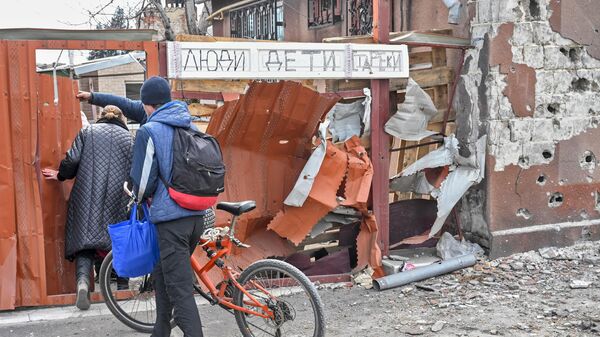 Жители Мариуполя идут к жилому дому, у ворот которого вывешена табличка с надписью Люди. Дети. Стареки