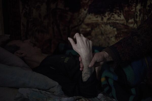 70-летняя Александра Чубарова держит за руку своего парализованного мужа 77-летнего Петра Чубарова. Александра и Петр - одни из последних жителей поселка Новомарьевка Донецкой области.