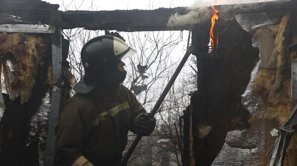 Сотрудник противопожарной службы ДНР тушит пожар в доме, обстрелянном из РСЗО Град ВСУ, в Ясиноватой
