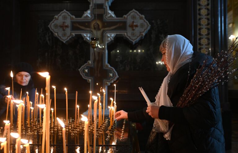 Женщина ставит свечу в праздник Вербного воскресенья в храме Христа Спасителя в Москве