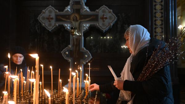 Женщина ставит свечу в праздник Вербного воскресенья в храме Христа Спасителя в Москве