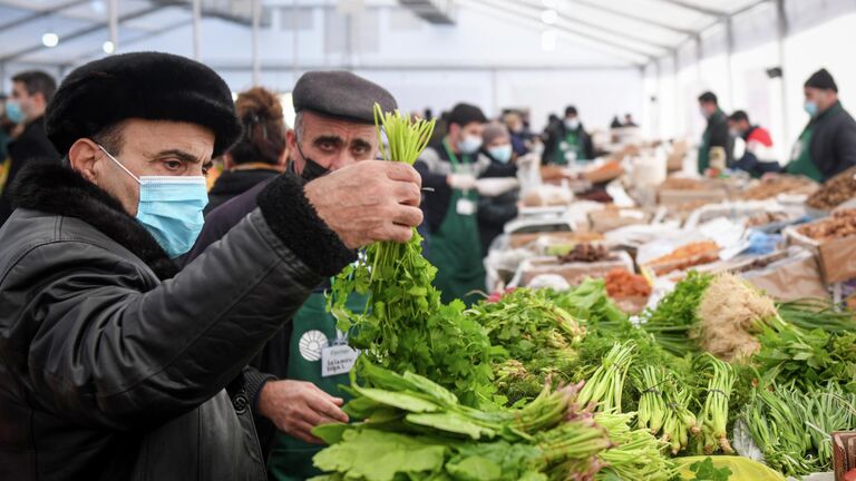Покупатель выбирает зелень на продуктовой ярмарке в Баку