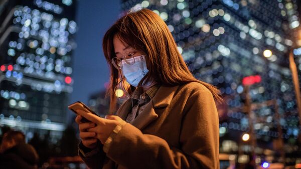 Женщина в маске смотрит в мобильный телефон, Пекин