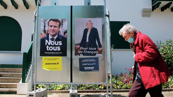 Женщина проходит мимо предвыборных плакатов кандидатов в президенты Эммануэля Макрона и Марин Ле Пен в Англе