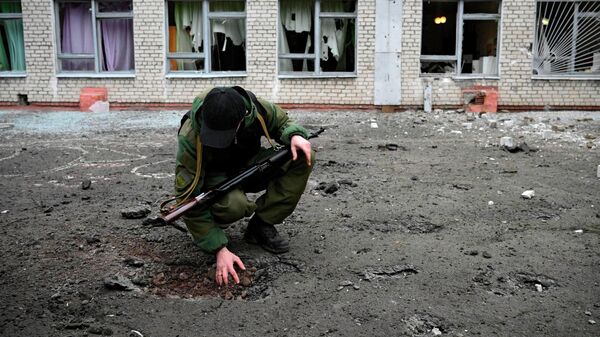 Сотрудник народной милиции ДНР возле воронки от снаряда у школы в Горловке