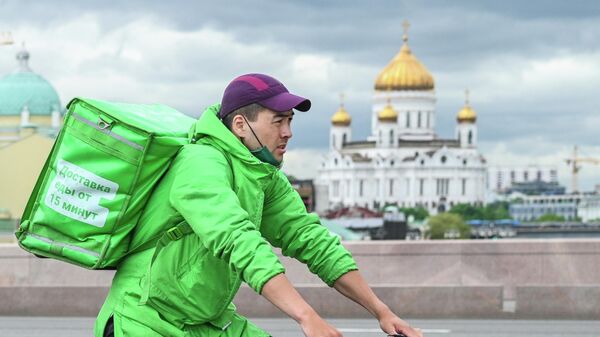 Курьер службы доставки Delivery Club едет на велосипеде на Большом Москворецком мосту