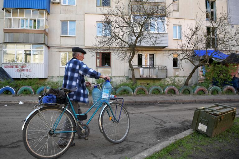 Мужчина везет бутылки для воды на велосипеде к месту раздачи в городе Рубежное Луганской народной республики