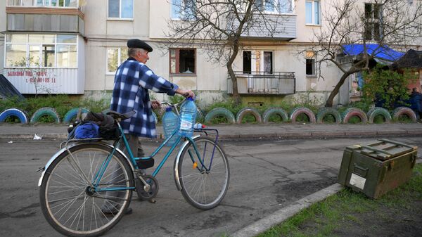Мужчина везет бутылки для воды на велосипеде к месту раздачи в городе Рубежное Луганской народной республики