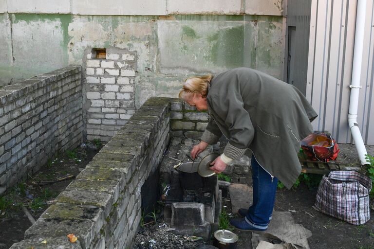 Женщина готовит еду возле подъезда жилого дома в городе Рубежное Луганской народной республики