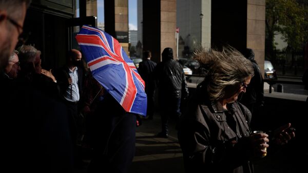 Человек идет под зонтом в цвете флага Великобритании в Лондоне 