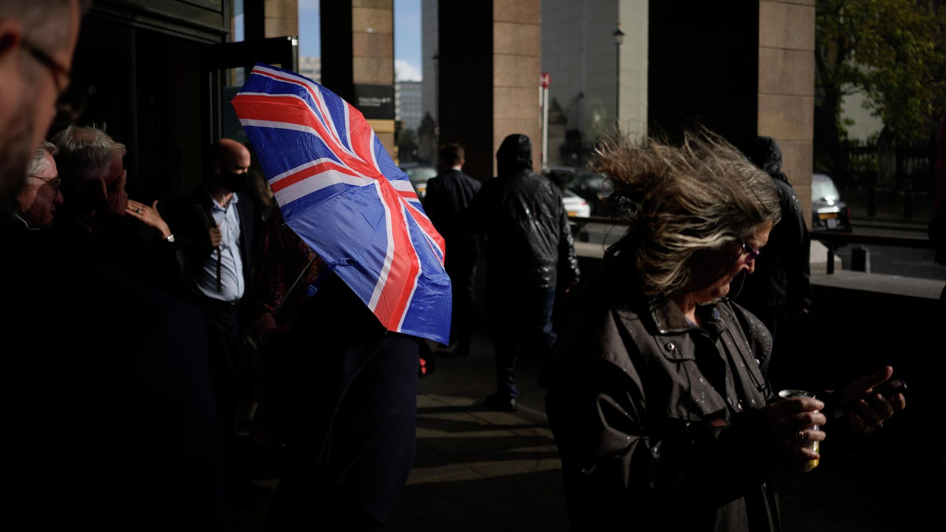 Человек идет под зонтом в цветах флага Великобритании в Лондоне - РИА Новости, 1920, 29.01.2024