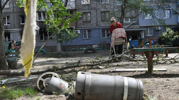 Жительница стирает одежду во дворе разрушенного дома в ДНР