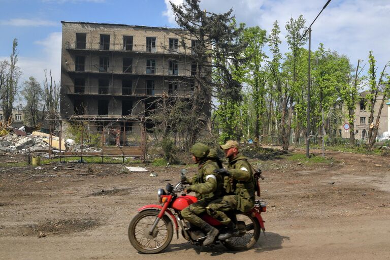 Военнослужащие едут на мотоцикле мимо разрушенных домов в городе Попасная