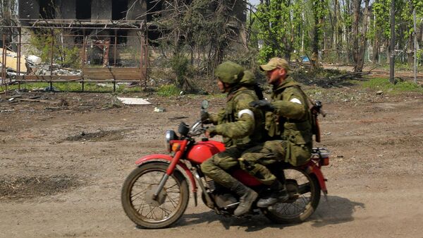 Военнослужащие едут на мотоцикле мимо разрушенных домов в городе Попасная