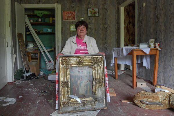 Женщина показывает поврежденную при обстрелах семейную икону в своем разрушенном доме в городе Попасная